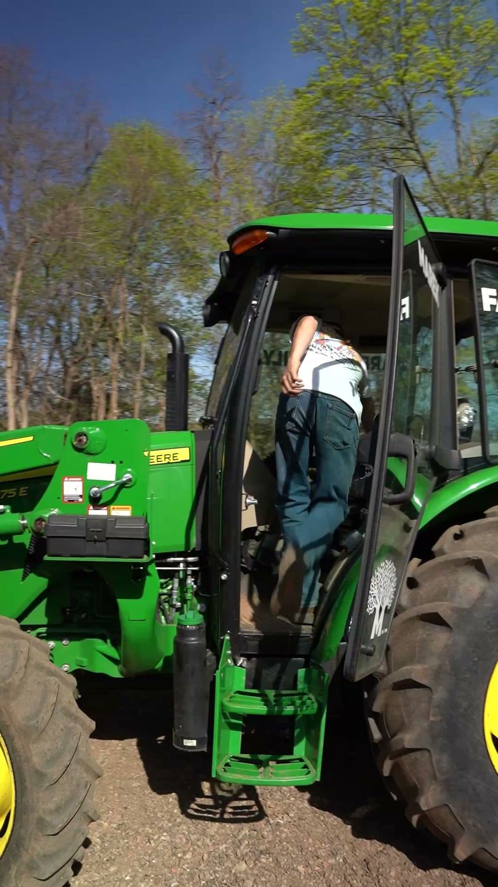Person climbing into a green tractor with bright yellow tires on a sunny day.