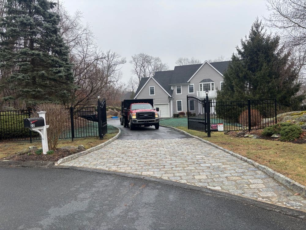 Driveway leading to a modern home with a red truck and gated entrance on a cloudy day.