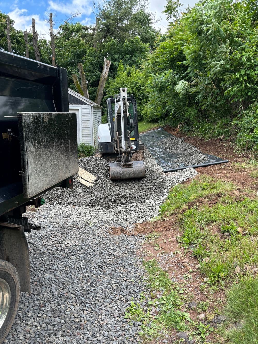 Excavator working on gravel pathway installation behind a house with landscaping.