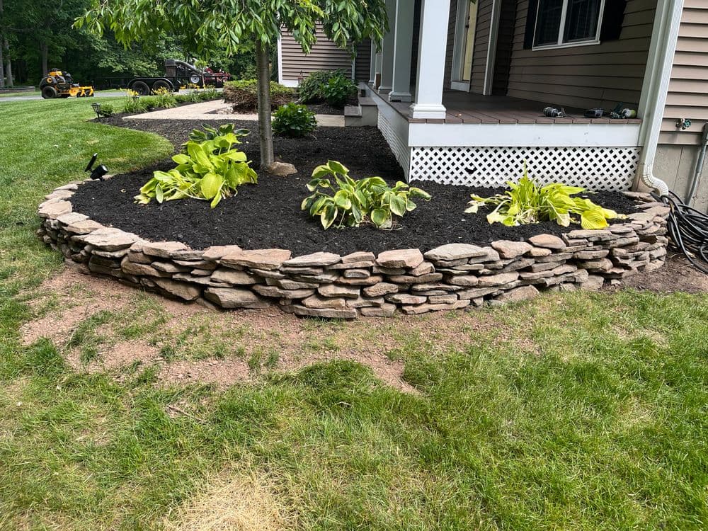 Stone retaining wall with lush green plants and fresh mulch in a landscaped yard.