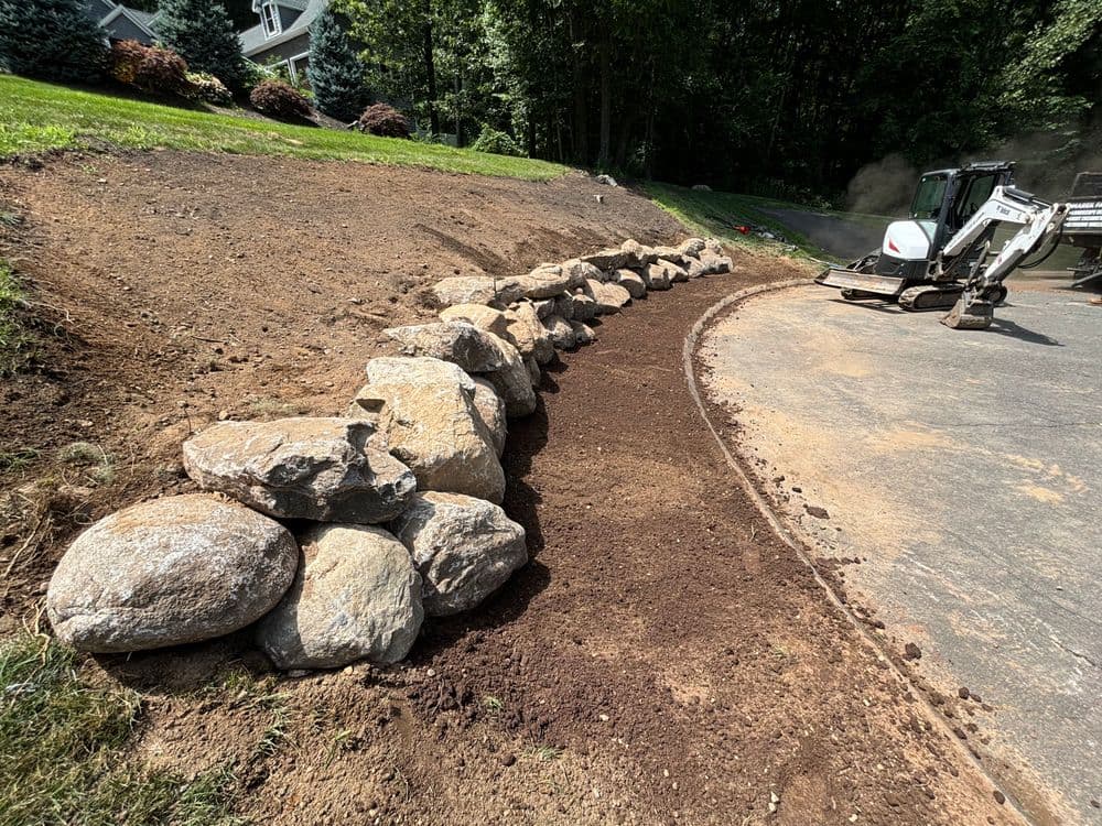 Landscaping project featuring large boulders forming a curved garden edge along a driveway.