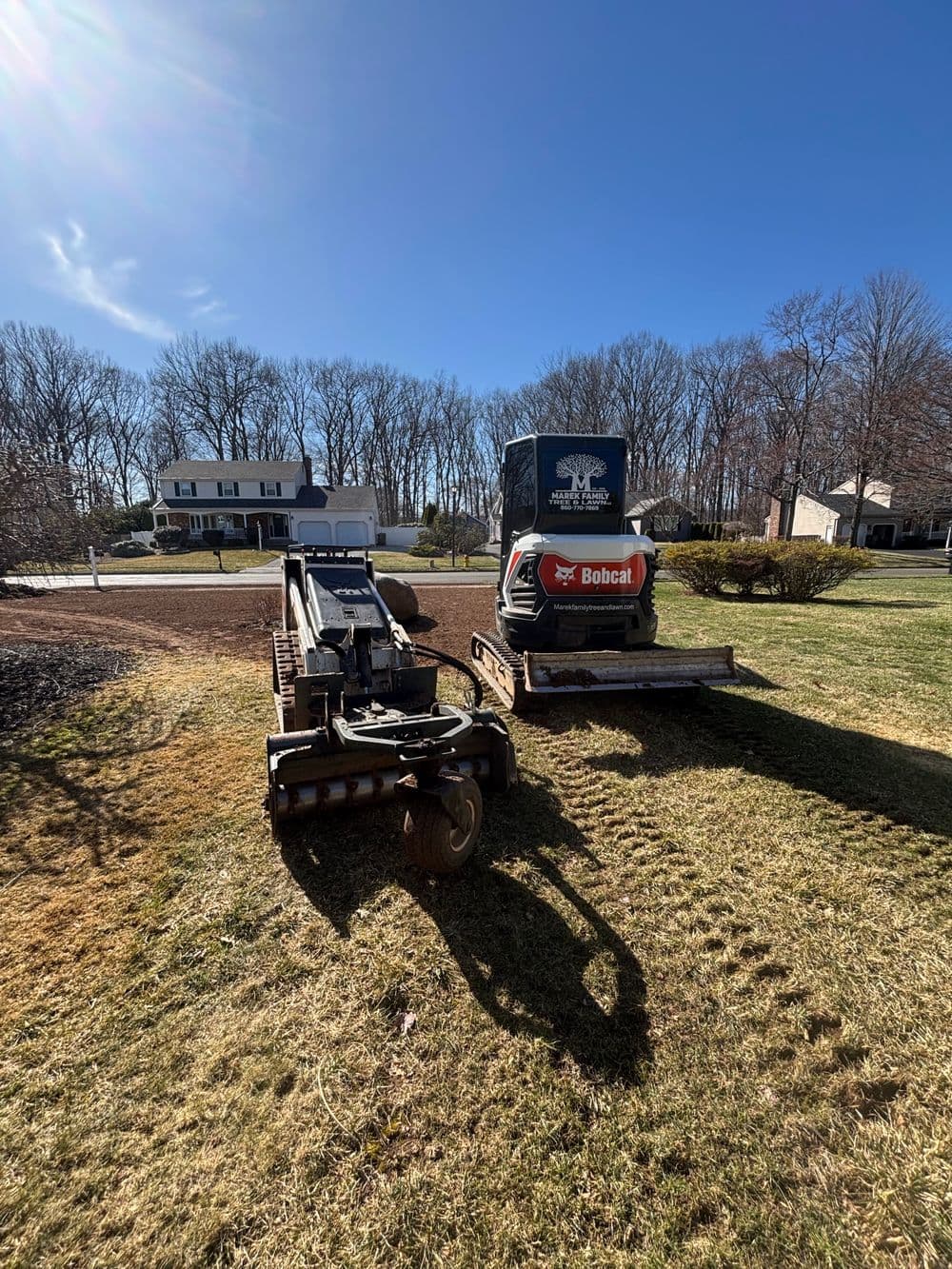 Skid steer loader parked on a flatbed trailer in a residential yard on a sunny day.
