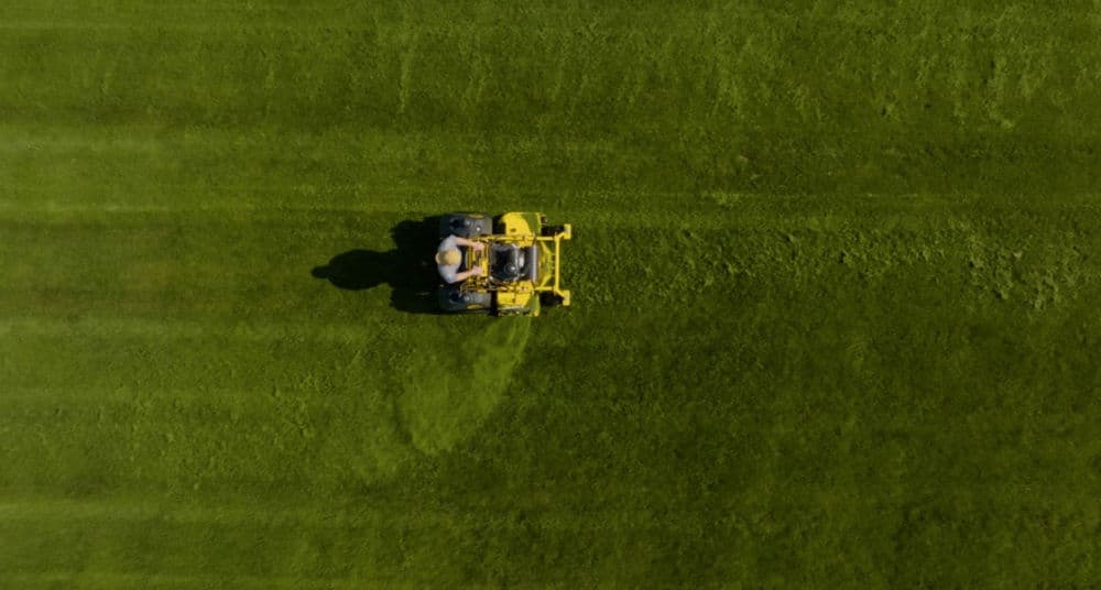 Aerial view of a lawn mower cutting fresh, green grass in a well-maintained field.