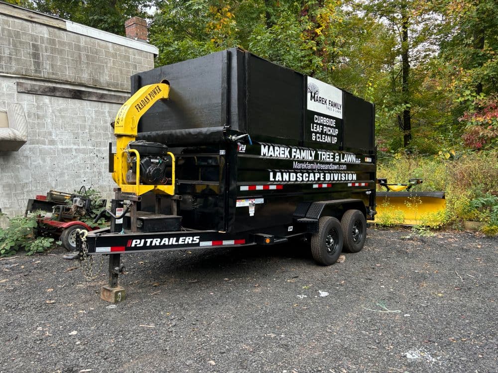 Marek Family Tree & Lawn Services trailer with landscape division equipment in a wooded area.