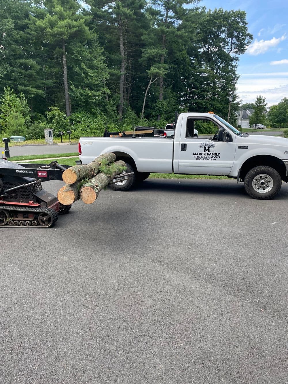 Pickup truck transporting logs with a mini skid steer on a residential road.
