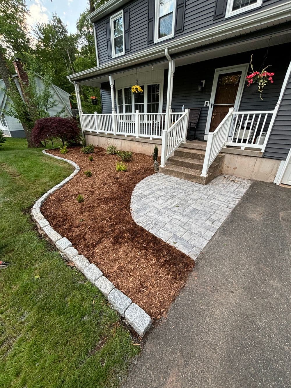 Front yard landscaping featuring a stone pathway, mulch, and garden plants near a house.