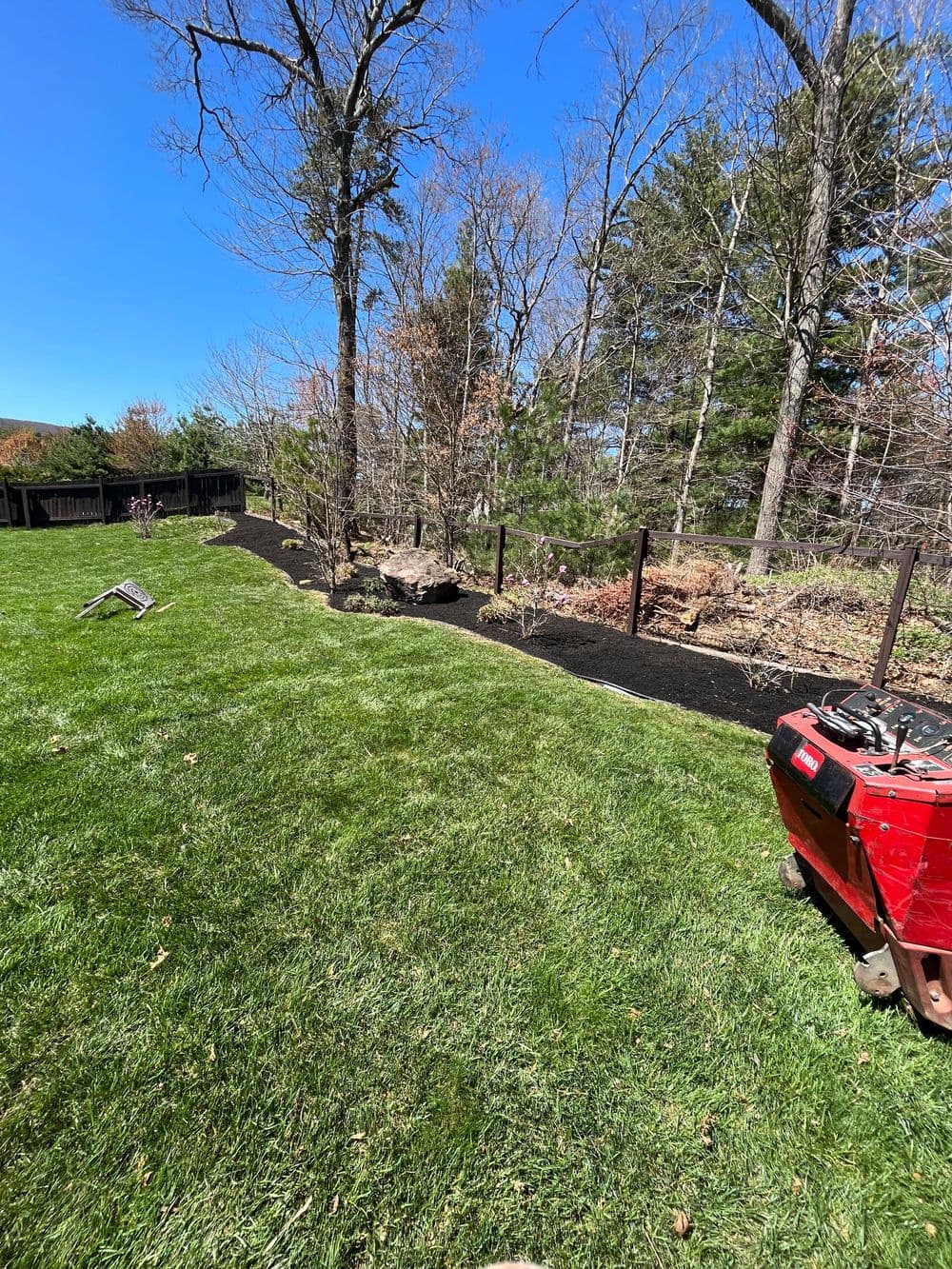 Lush green lawn with a recently landscaped garden and clear blue sky in the background.