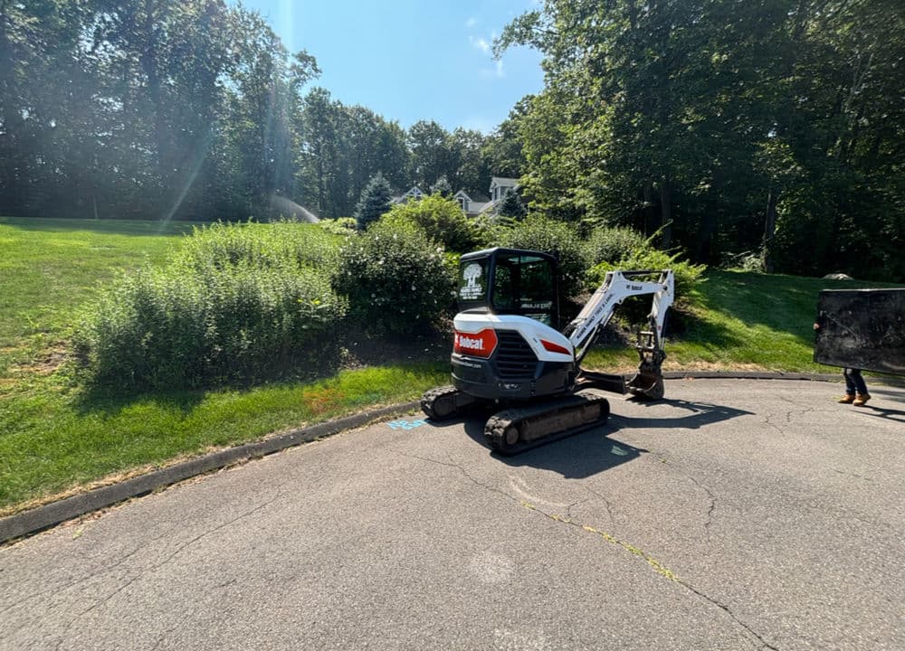 Compact excavator on a road near a grassy hillside, preparing for landscaping work.