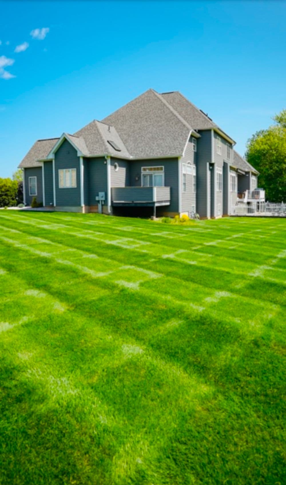 Beautiful gray house with manicured green lawn and blue sky in the background.