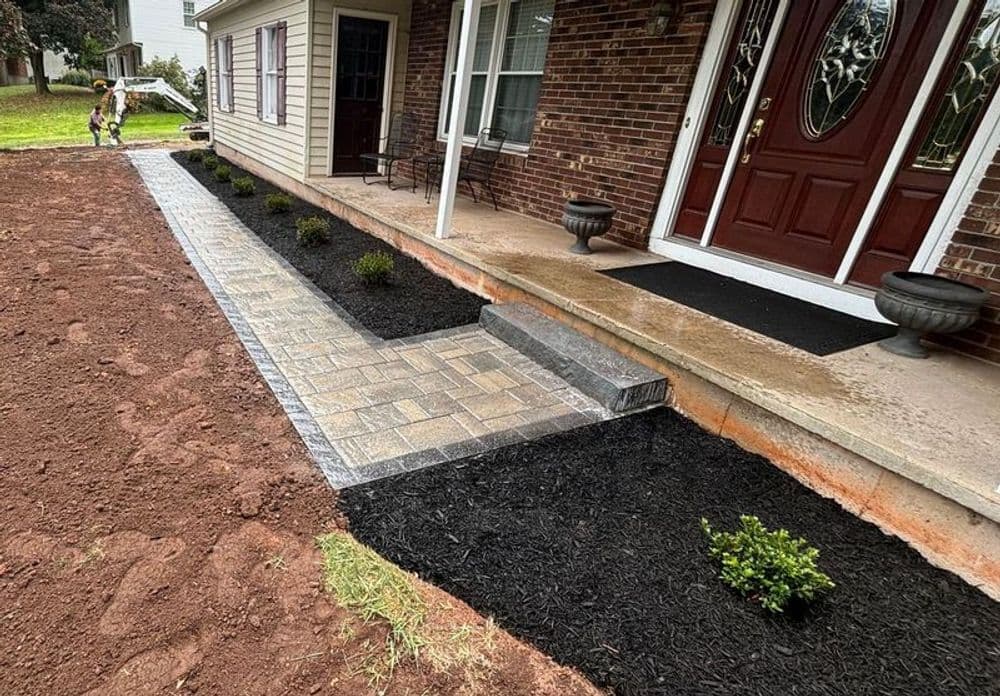 Newly landscaped front entrance with paver walkway, black mulch, and plants.